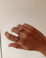 Anillo ajustable de metal dorado con dije de cruz decorado con pequeños cristales brillantes.