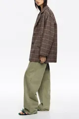 Abrigo de corte sastrero con diseño a cuadros en tonos marrones y grises. Presenta silueta estructurada, cuello con solapas, cierre frontal con botones y bolsillos laterales. Las solapas y los bordes cuentan con un acabado desflecado que le otorga un estilo contemporáneo.