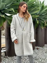 Sacón largo de punto color crudo, con cuello solapa, un botón frontal, mangas largas con puños doblados y dos bolsillos delanteros.