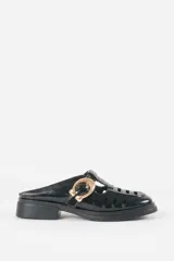 Zuecos negros de charol estilo mocasín destalonado, con perforaciones laterales tipo huarache, tacón bajo cuadrado y hebilla metálica dorada decorativa en el empeine.