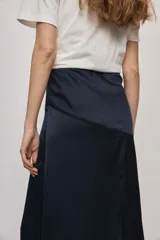 Falda larga de color negro, calce al cuerpo y caída fluida, confeccionada en tejido satinado con detalle de recorte diagonal en la parte delantera y cintura elástica.