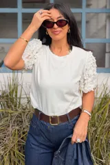 Remera blanca de algodón con mangas cortas abullonadas decoradas con apliques de flores en relieve. Presenta cuello redondo y un diseño versátil ideal para diversas ocasiones.