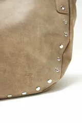 Cartera beige con tachas plateadas, doble asa de hombro con detalle trenzado y herrajes metálicos.