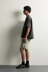 Bermuda cargo color negro de corte relaxed fit, confeccionada en tejido de algodón con elasticidad y efecto lavado. Cuenta con cintura elástica ajustable con cordón, bolsillos frontales y bolsillos laterales tipo cargo con solapa en las perneras.