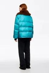 Campera acolchada corta de tejido técnico en color turquesa, con cierre frontal de cremallera y botones de presión. Presenta cuello con detalle de pelo sintético desmontable, bolsillos frontales con tapeta y bolsillo con cierre en la manga.