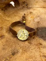 Pulsera con dije redondo dorado con diseño abstracto y cinta de terciopelo elástico color gris claro.