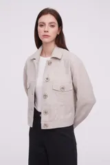 Chaqueta corta color arena melange con cuello camisero, cierre frontal con botones dorados y bolsillos de parche en el pecho.