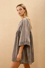 Vestido corto de algodón color gris lavado, con escote en V y cordones ajustables. Presenta mangas anchas tipo murciélago y bordados florales en el canesú.