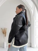 Buzo negro de ecocuero con cuello polo, cierre frontal con cremallera dorada y puños con elástico.