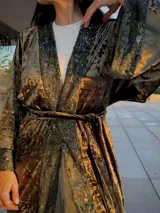 Kimono de terciopelo verde con detalles de lentejuelas en los bordes frontales y en los puños. Presenta un diseño de manga larga amplia, corte holgado y lazo ajustable en la cintura.
