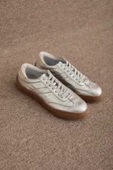 Zapatillas urbanas de cuero metalizado plateado con suela de goma color suela y detalle en el talón en tono crema.