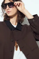 Sobrecamisa tipo Barn Jacket color marrón oscuro, de algodón con elastano, silueta relajada y estructura firme. Presenta cierre frontal con botones metálicos, cuello negro, bolsillos aplicados y pespuntes visibles.