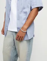 Pulsera con cuentas peque
nas de aleaci
f3n de metales ba
f1adas en plata de ley, con cierre de cuero marr3n.