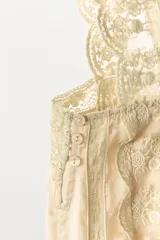 Top de estilo corset confeccionado en viscosa satinada color beige. Presenta escote recto, tirantes anchos con terminación de encaje, detalle de pliegues verticales, lazada frontal y aplicaciones de encaje con bordados florales en el cuerpo y el ruedo.