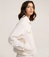 Campera trucker confeccionada en sarga de algodón color blanco, con cuello tradicional, cierre frontal de botones metálicos, bolsillos frontales con solapa y costuras reforzadas.