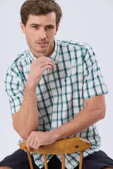 Camisa de manga corta a cuadros en tonos blanco, azul y gris, con cuello abotonado, bolsillo en el pecho y cierre frontal con botones.