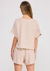 Blusa corta de lino y viscosa color beige, con escote redondo, mangas cortas holgadas tipo mariposa y detalles de bordado festoneado en contrastes blancos en el cuello, puños y ruedo.