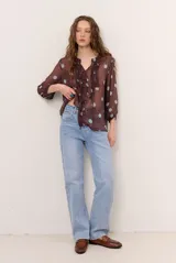 Blusa marrón semitransparente con estampado de lunares celestes, mangas largas abuchonadas, cuello en V con lazos y detalles de volados frontales.