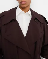 Gabardina oversize color marrón oscuro, con diseño cruzado, solapas grandes, mangas largas con trabilla en los puños, bolsillos delanteros y cinturón ajustable del mismo tejido.