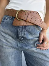 Cinto tipo faja color camel, confeccionado en cuero sintético, con diseño de tachas metálicas circulares y hebilla redonda en tono bronce envejecido.