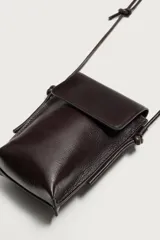 Bandolera porta teléfono de piel marrón con acabado liso, compartimento principal con solapa imantada y asa de hombro ajustable con nudos.