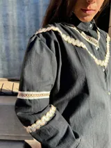 Camisa blanca de mangas largas con detalles de puntilla beige en cuello y puños, y cierre frontal con botones.