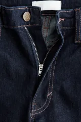 Jean de tiro alto con corte acampanado desde la rodilla, confeccionado en denim oscuro con cinco bolsillos y cierre frontal con botón.