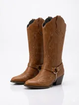 Bota estilo texana de caña alta, color tostado, con bordados decorativos en el cuerpo y puntera fina. Presenta una tira ajustable con hebilla y una cadena metálica colgante en el tobillo, con taco cuadrado de altura media.