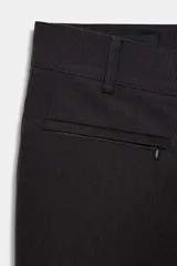 Pantalón entallado de tiro alto color negro, con cintura con trabillas y bolsillos de vivo con cremallera en el delantero. El bajo tiene un acabado en línea evasé. Cierre frontal con cremallera, botón interior y gancho metálico.