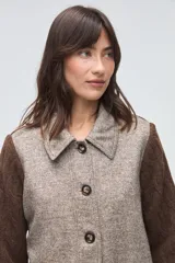 Trench de lana fina sin teñir, con diseño de textura combinada. Presenta mangas y espalda tejidas con patrón de trenzas, cuerpo liso, cuello camisero, cierre frontal con botones y bolsillos delanteros funcionales.