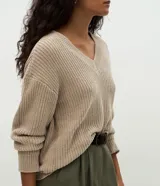 Suéter de punto color beige con escote en V, mangas largas con puños ajustados y diseño holgado. Confeccionado en poliéster.
