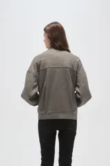 Campera de corte holgado en color gris, con cuello alto, cierre frontal oculto y mangas largas. Presenta costuras decorativas en el frente y bolsillos laterales.