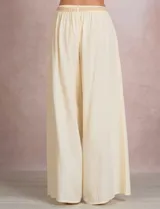 Pantalón palazzo de tiro alto marca Elan, en color beige, confeccionado en mezcla de algodón, viscosa y lino. Presenta cintura delantera plana con parte trasera elastizada, bolsillos laterales funcionales y corte de pierna ancha. Incluye un cinturón trenzado al tono con terminación en borlas y flecos.