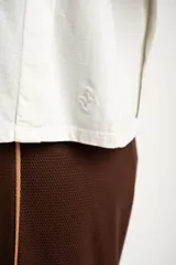 Remera de algodón color mostaza/naranja quemado, con cuello redondo y mangas cortas. Presenta un diseño con costuras externas visibles en los hombros y laterales, dándole un aspecto desestructurado.