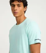 Remera deportiva de hombre con tecnología dry fit, cuello redondo y manga corta. Presenta un diseño liso en color beige con una pequeña etiqueta decorativa en el dobladillo.