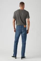 Jean de corte slim fit con tiro bajo, confeccionado en denim azul con efecto de lavado desgastado. Presenta cierre de botones y remaches metálicos clásicos.