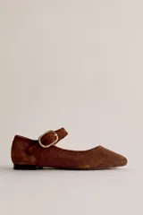 Mocasín de gamuza color marrón, con diseño plano, punta cuadrada y tira en el empeine con hebilla metálica dorada.