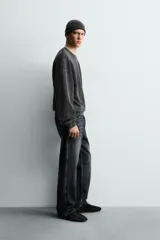 Sudadera de corte relajado, color negro con efecto lavado, cuello redondo y manga larga. Presenta un pequeño estampado frontal con texto en tonos naranja y amarillo.