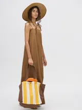 Vestido midi de denim color marrón, con corte holgado, breteles finos con lazos ajustables y detalle de volado en el ruedo.