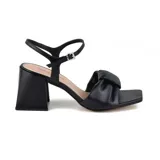 Sandalia de cuero sintético color negro, con taco cuadrado, tira ancha sobre el empeine con detalle de nudo y pulsera al tobillo con hebilla.