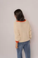 Sweater tejido color crema con cuello y puños acanalados en color naranja. Presenta un diseño bordado de un perro salchicha negro con un moño naranja.