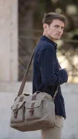 Bolso tipo maletín de tela canvas color beige con detalles en cuero sintético marrón. Cuenta con dos bolsillos frontales con tapa y cierre de hebilla, cierre superior, doble asa de mano y correa larga ajustable y desmontable.