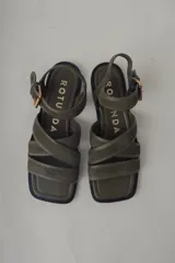 Sandalia plana de cuero negro, con diseño minimalista de tiras finas cruzadas sobre el empeine y una tira ajustable con hebilla metálica en el tobillo.