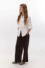 Camisa beige de manga larga, con cuello clásico, botones marrones y dos bolsillos frontales. Presenta costuras decorativas en contraste.