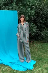 Conjunto de camisa y pantalón de fibrana con diseño a rayas verticales en tonos verde, blanco, violeta y negro. La camisa es de corte amplio con bolsillos frontales en el pecho, y el pantalón es de corte recto y holgado.