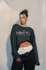 Crewneck (jersey de cuello redondo) unisex color gris oscuro, con estampado frontal que dice "RE:SKIN" y texto pequeño debajo. Presenta mangas largas y corte holgado.