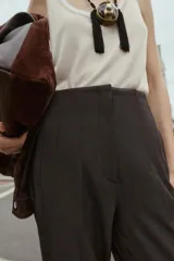 Pantalón de tiro alto color beige, con detalle de costuras marcadas en el delantero y la espalda. Incluye bolsillos delanteros de vivo y cierre frontal con cremallera, botón interior y gancho metálico.