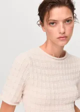 Jersey de punto de manga corta con diseño entallado, cuello redondo y detalle de volante en el bajo. Presenta una textura sutil en el tejido.