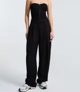 Pantalón de sastrería corte barrel, color marrón oscuro, con pliegues delanteros, cintura con cierre desplazado y piernas anchas.