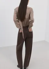 Blusa de manga larga con estampado de rayas verticales en tonos marrones y crema. Presenta un cuello alto con una corbata integrada del mismo tejido y cierre frontal de botones ocultos.